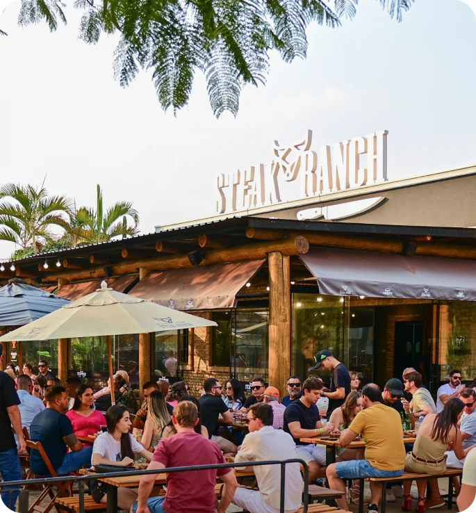 Clientes nas mesas externas de uma unidade Steak Ranch durante o dia, modelo de loja da franquia
